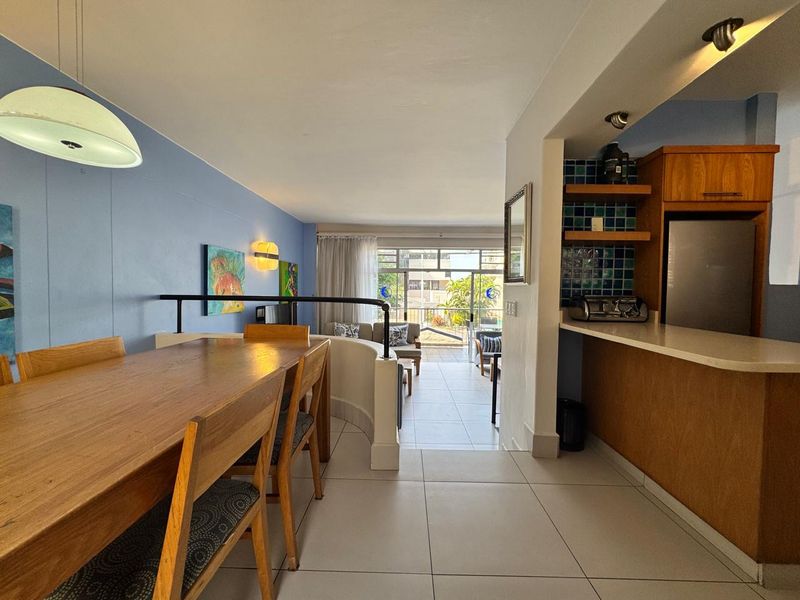 Open-plan living and dining area featuring tiled floors, a breakfast bar, and direct access to a balcony through sliding glass doors.