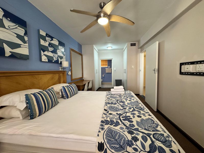 A well-maintained bedroom featuring a ceiling fan, built-in cupboards, and an integrated vanity area with direct access to an en-suite bathroom.
