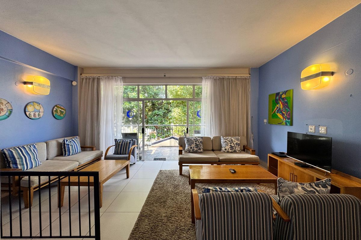 Spacious living room featuring tiled flooring, wall-mounted lighting, and large sliding glass doors providing access to an outdoor area.