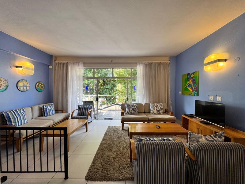 Spacious living room featuring tiled flooring, wall-mounted lighting, and large sliding glass doors providing access to an outdoor area.