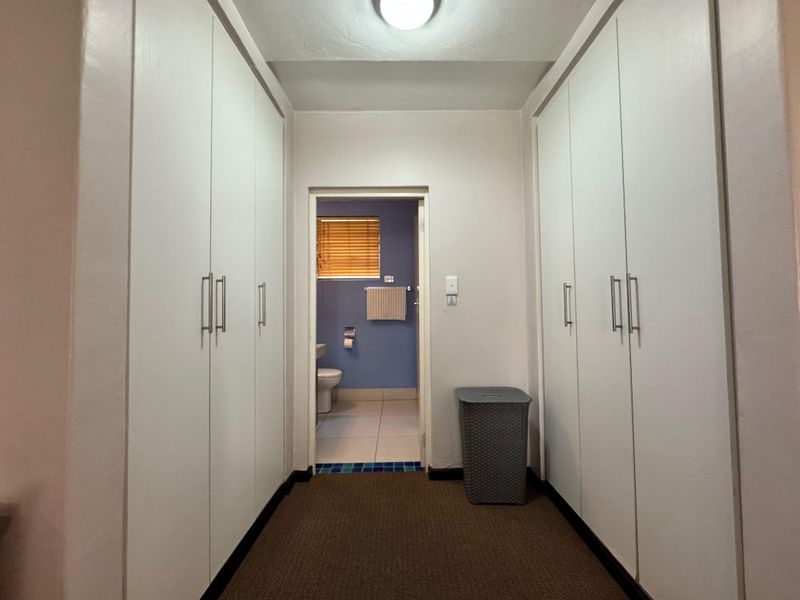 A functional hallway featuring extensive built-in cupboard storage, leading directly into a bathroom with tiled flooring.