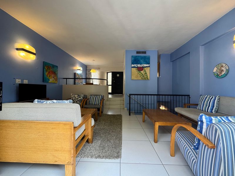 A split-level living area featuring tiled flooring, blue painted walls, and a metal stair railing leading to the entrance.