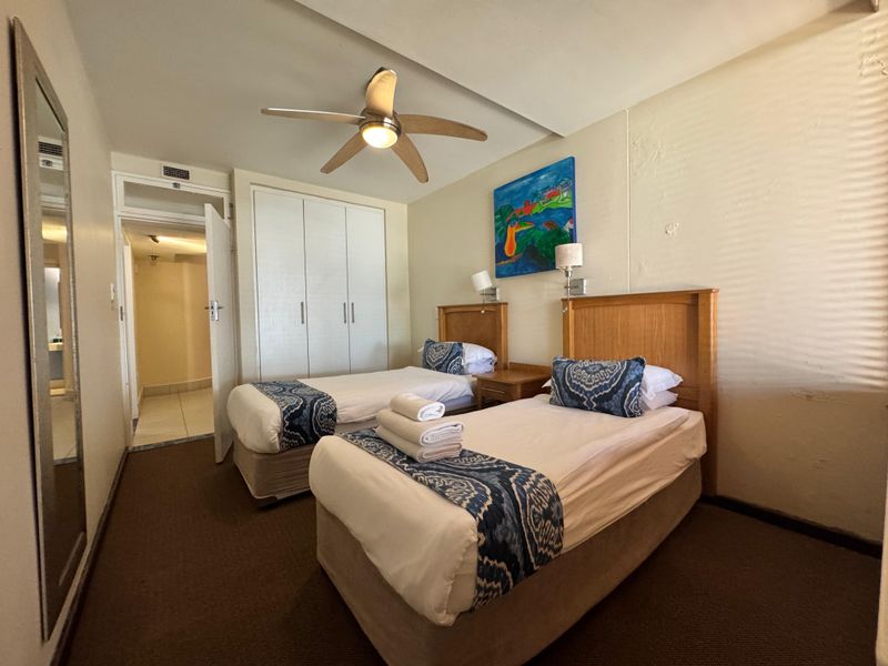 A functional bedroom featuring built-in cupboards, a ceiling fan, and wall-mounted lighting, with direct access to an adjoining bathroom.