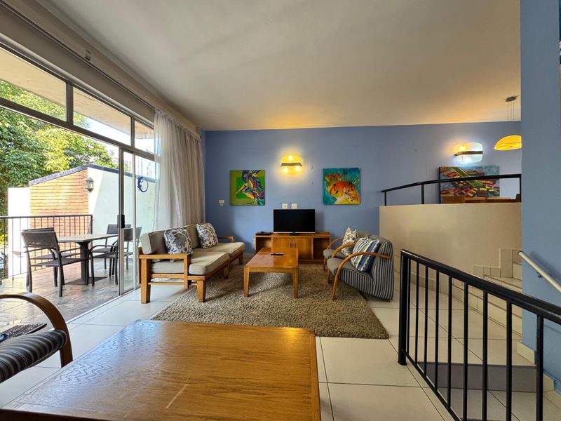 Spacious living area featuring large sliding glass doors leading to a balcony, tiled flooring, and an open-plan layout with staircase access.
