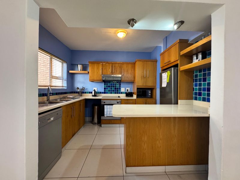 Functional kitchen featuring wooden cabinetry, tiled splashbacks, a breakfast bar, and integrated appliances, offering a practical layout for daily use.