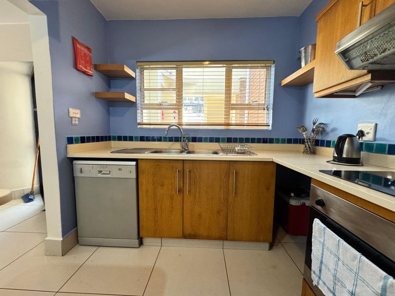 A functional kitchen featuring wooden cabinetry, tiled splashbacks, built-in oven with extractor fan, and tiled flooring, offering a practical layout for daily use.