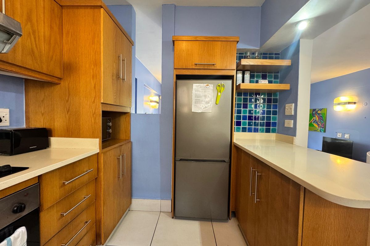 A functional kitchen featuring wooden cabinetry, stone countertops, a built-in oven, and a vibrant blue tiled backsplash, offering a practical layout for daily use.