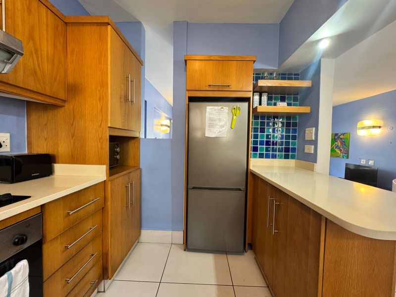 A functional kitchen featuring wooden cabinetry, stone countertops, a built-in oven, and a vibrant blue tiled backsplash, offering a practical layout for daily use.