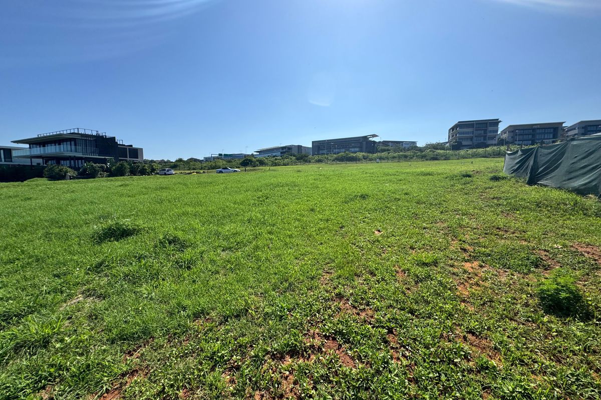 A wide-angle view of a vacant residential plot featuring open grass terrain and surrounding neighborhood development.