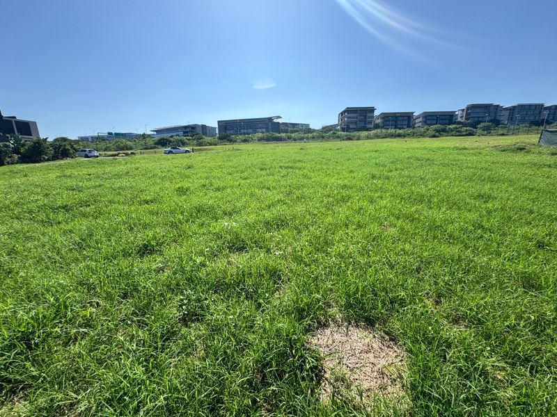 A wide-angle view of a vacant residential plot featuring a well-maintained grass lawn and perimeter fencing in a developed neighborhood.