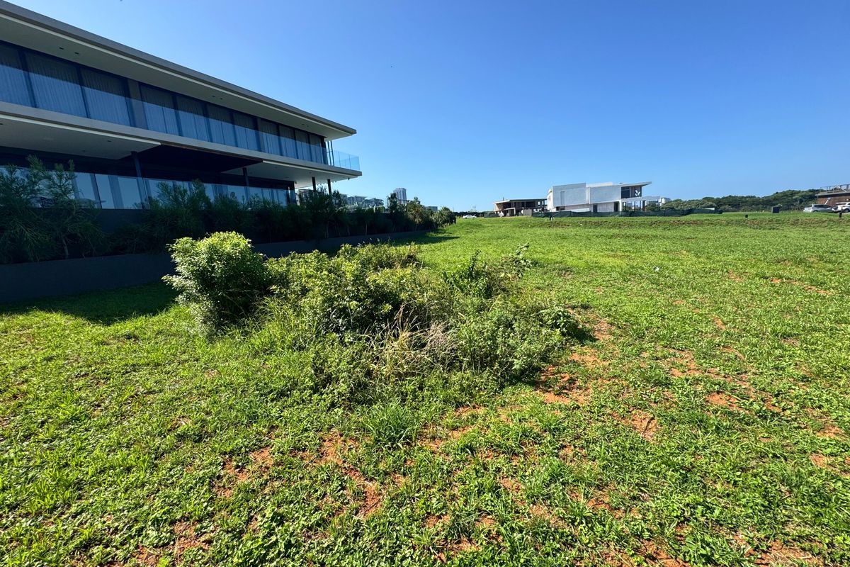 A view of the vacant residential land plot, featuring open grass areas with neighbouring modern architectural structures visible in the background.