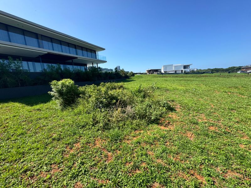 A view of the vacant residential land plot, featuring open grass areas with neighbouring modern architectural structures visible in the background.