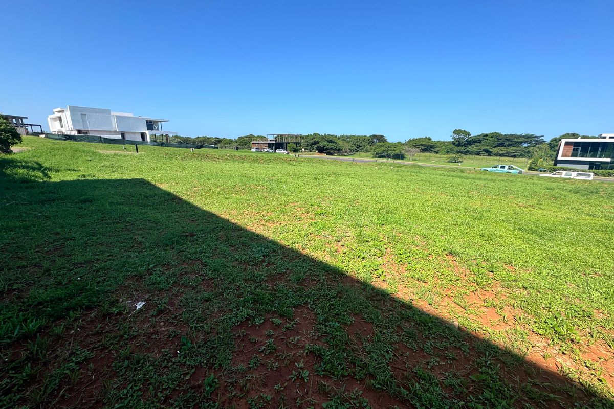 A wide-angle view of a vacant residential plot featuring a well-maintained grass lawn and surrounding neighborhood development.