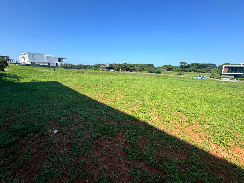 A wide-angle view of a vacant residential plot featuring a well-maintained grass lawn and surrounding neighborhood development.