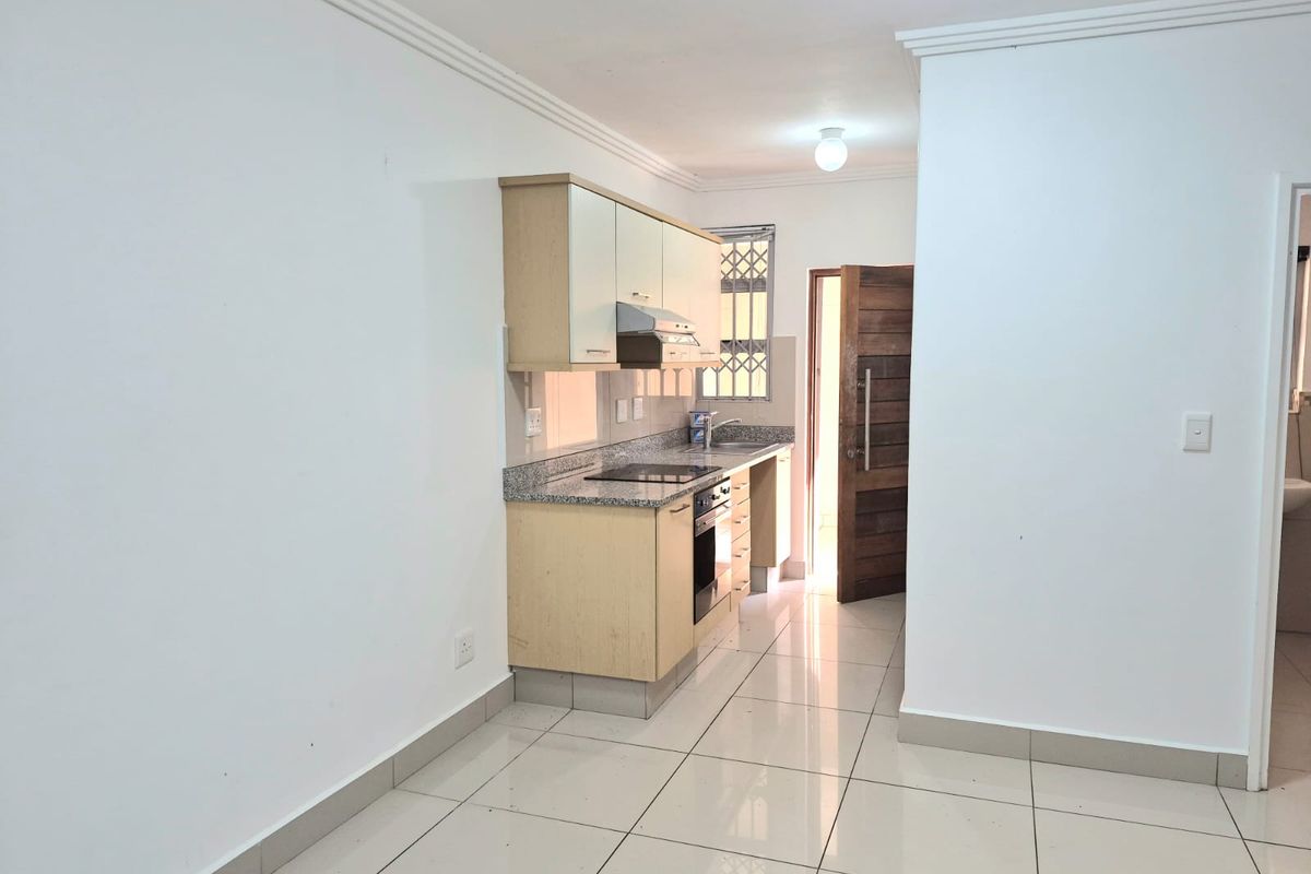 Compact kitchen featuring light wood cabinetry, granite countertops, built-in oven and hob, and polished tile flooring.