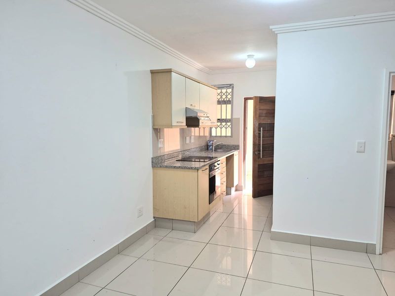 Compact kitchen featuring light wood cabinetry, granite countertops, built-in oven and hob, and polished tile flooring.