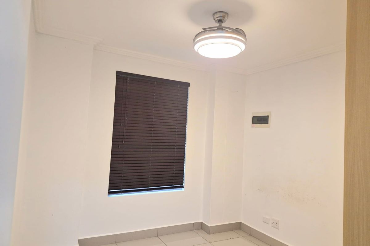 An empty bedroom featuring tiled flooring, a ceiling fan, and dark venetian blinds. The space includes a wall-mounted electrical distribution board.
