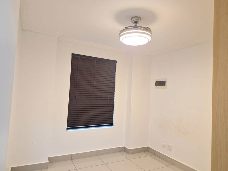 An empty bedroom featuring tiled flooring, a ceiling fan, and dark venetian blinds. The space includes a wall-mounted electrical distribution board.