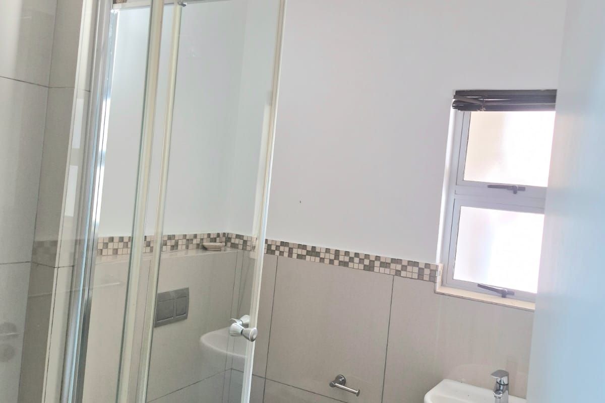 A clean and modern bathroom featuring a glass shower enclosure, wall-mounted toilet, and a wall-hung basin with neutral tiling.
