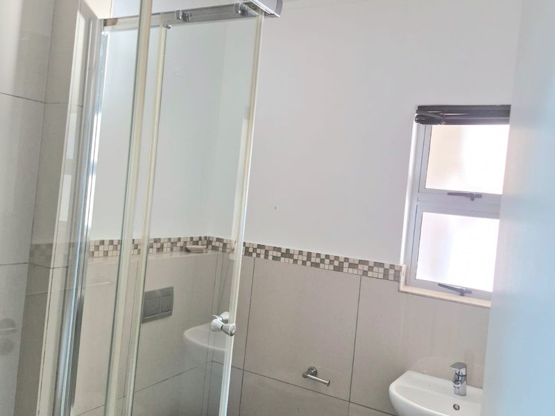A clean and modern bathroom featuring a glass shower enclosure, wall-mounted toilet, and a wall-hung basin with neutral tiling.