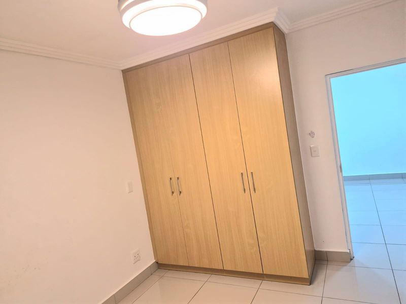 A clean, empty bedroom featuring light wood-finish built-in wardrobes, neutral tiled flooring, and a simple ceiling light fixture.