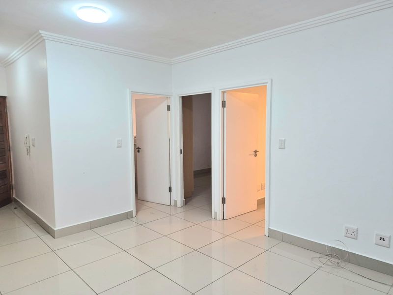 A clean, empty hallway featuring neutral tiled flooring, white walls, and multiple doorways leading to adjacent rooms within the apartment.