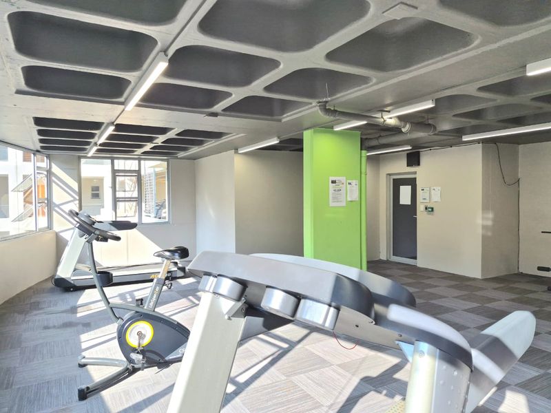 A functional apartment complex gym featuring a distinctive waffle slab ceiling, carpet tile flooring, and large windows providing natural light.