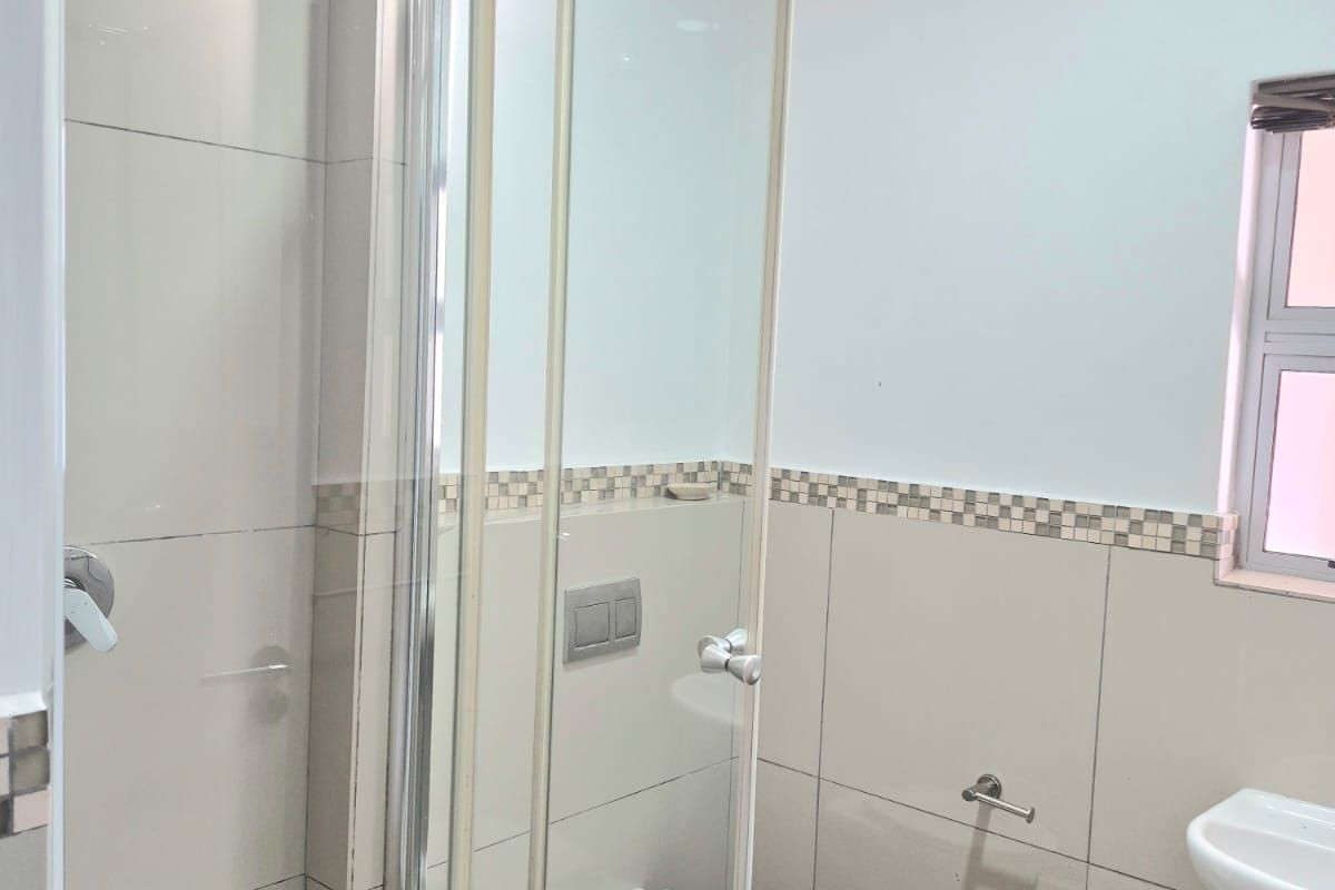 A clean, modern bathroom featuring a wall-mounted toilet, a glass-enclosed shower, and a wall-mounted basin with neutral ceramic tiling.
