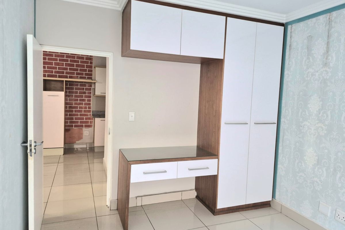 A clean bedroom featuring a modern built-in wardrobe with an integrated desk, tiled flooring, and neutral finishes, offering a functional and organized living space.