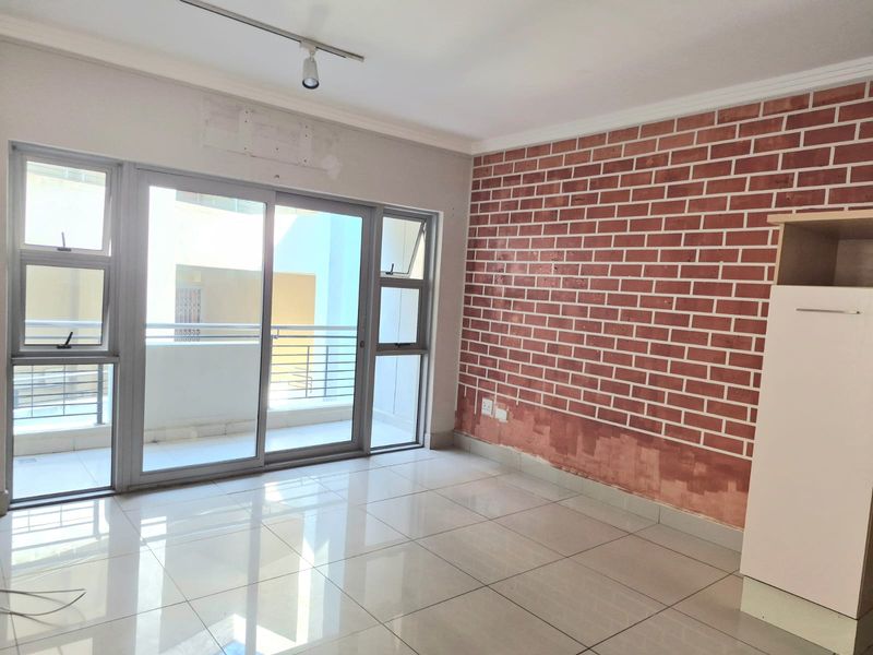 Bright living area featuring large sliding glass doors leading to a balcony, polished tile flooring, and a decorative exposed brick feature wall.