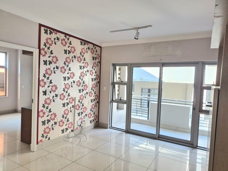An empty living room featuring tiled flooring, a floral feature wall, and sliding glass doors providing access to a balcony.