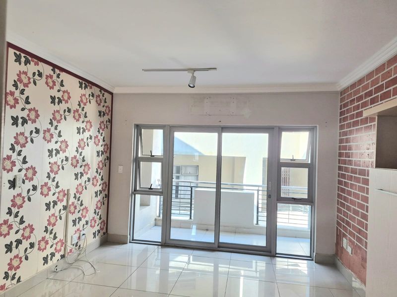 An empty living room featuring tiled floors, a sliding glass door leading to a balcony, and decorative feature walls.