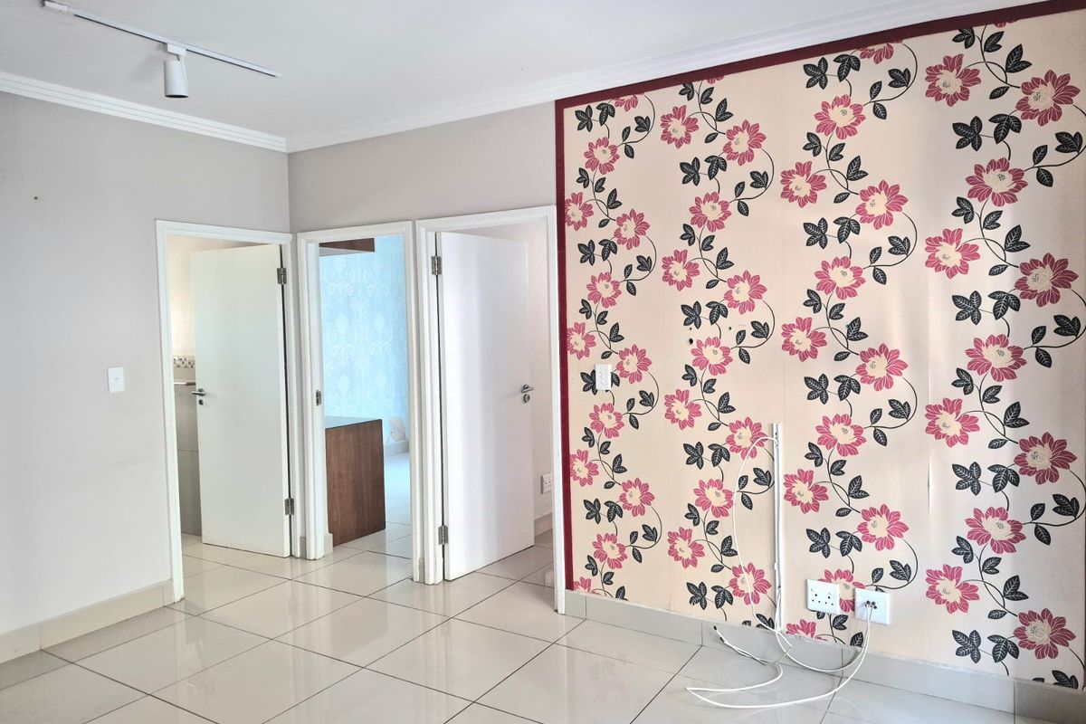 An empty living area featuring ceramic floor tiles, track lighting, and a decorative floral feature wall requiring maintenance or replacement.