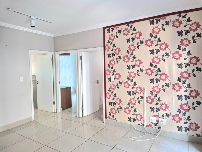 An empty living area featuring ceramic floor tiles, track lighting, and a decorative floral feature wall requiring maintenance or replacement.