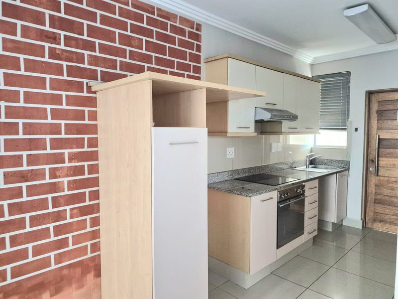 Modern kitchen featuring granite countertops, built-in oven and hob, ample cabinetry, and a distinctive brick feature wall.
