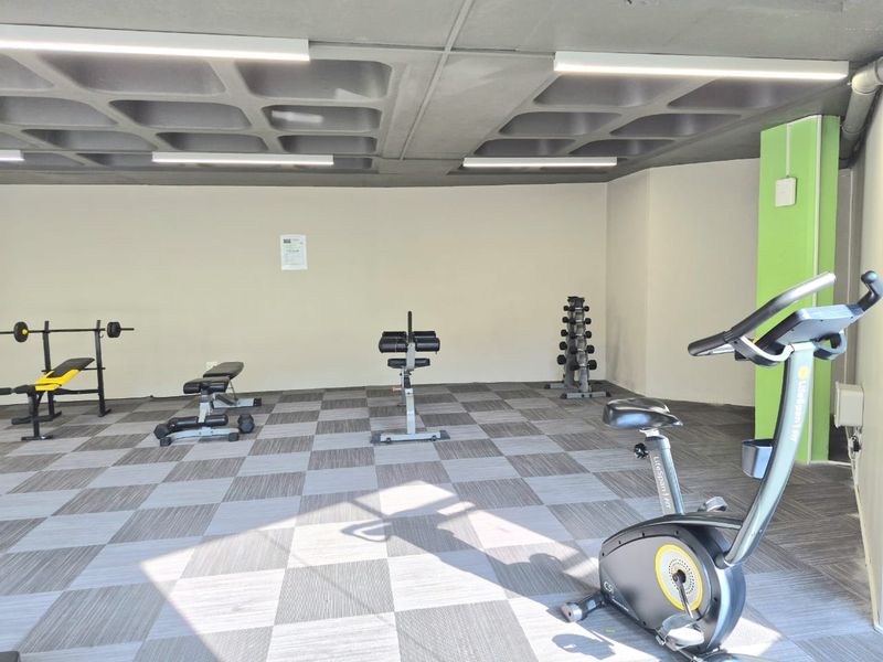 A functional apartment gym facility featuring a waffle slab ceiling, linear lighting, and durable carpet tile flooring.