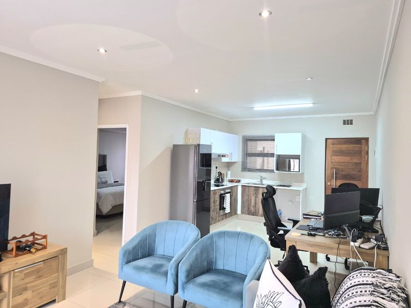 Open-plan living area featuring a modern kitchen with built-in cabinetry, integrated appliances, and tiled flooring, seamlessly connecting to the living and workspace areas.