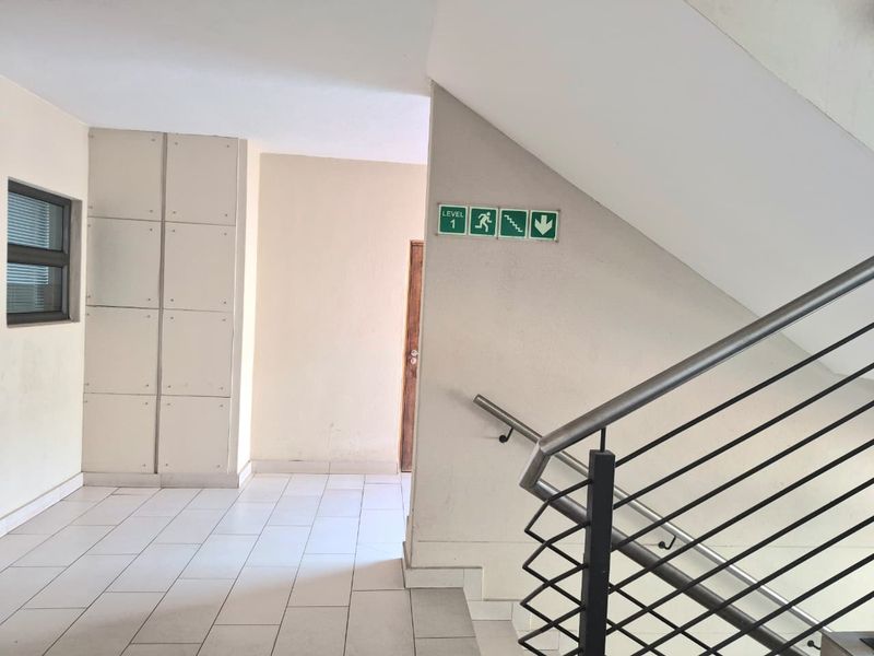A clean and functional apartment hallway featuring tiled flooring, built-in storage cupboards, and a metal staircase railing with clear emergency exit signage.