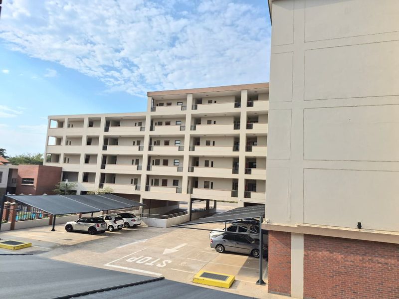 Exterior view of a multi-story apartment complex featuring covered parking bays and private balconies for each unit.