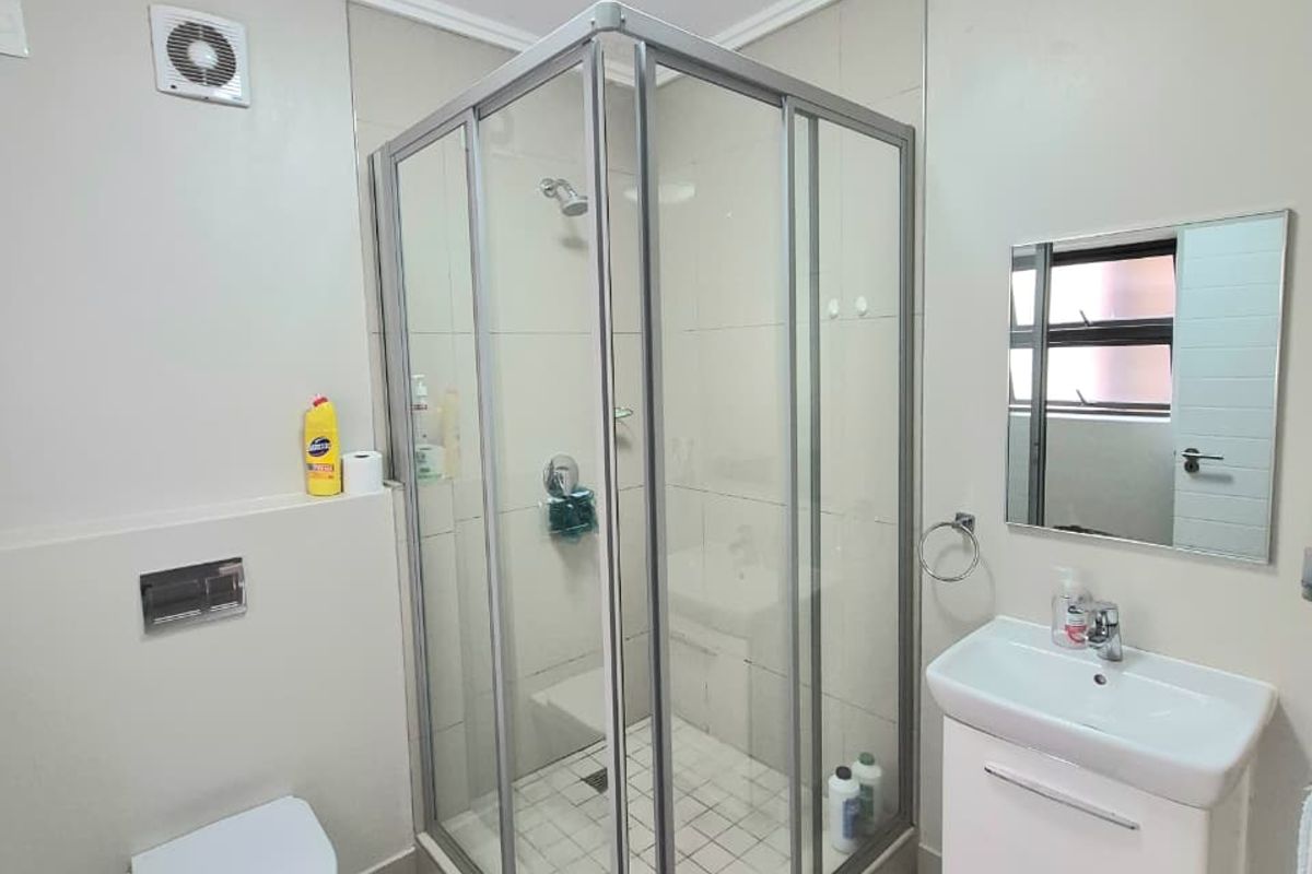 Modern bathroom featuring a corner shower enclosure, wall-mounted toilet, and a vanity basin with neutral wall and floor tiling.