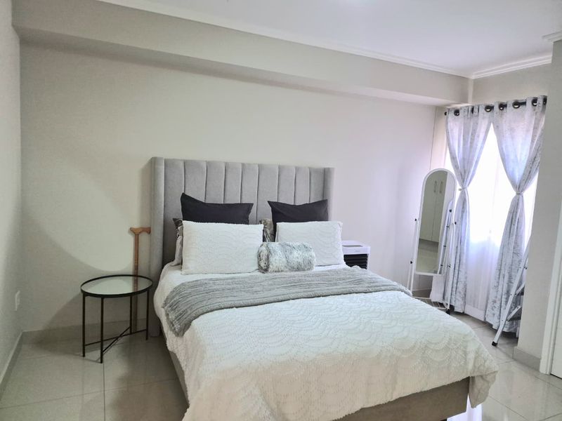 A well-maintained bedroom featuring neutral wall tones, tiled flooring, and natural light through window curtains.