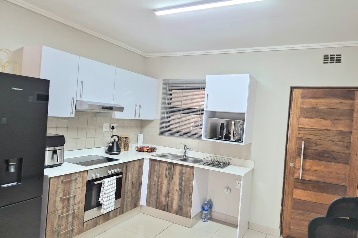 Modern kitchen featuring two-tone cabinetry, built-in oven and hob, extractor fan, double sink, and tiled flooring with direct access to a wooden door.