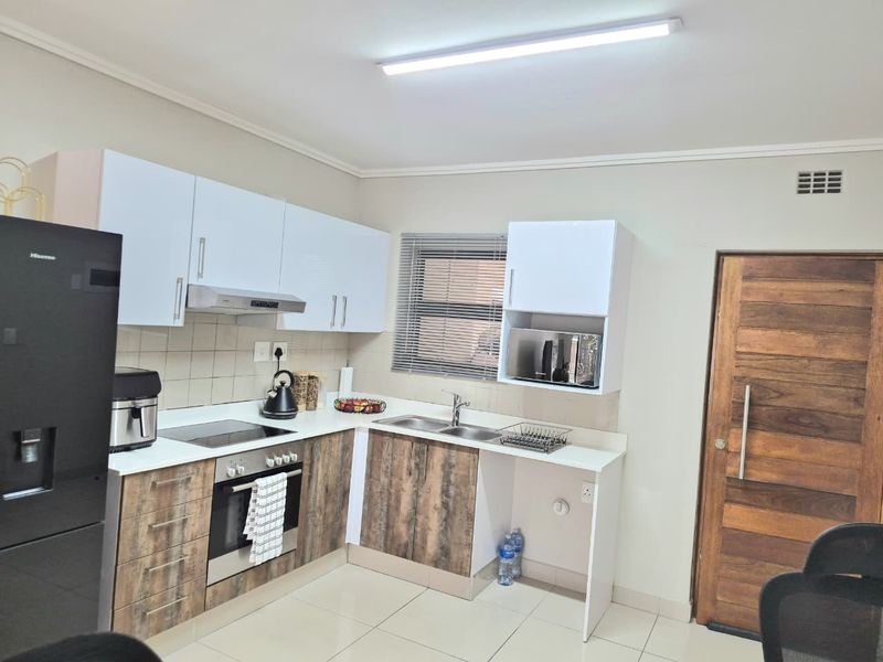 Modern kitchen featuring two-tone cabinetry, built-in oven and hob, extractor fan, double sink, and tiled flooring with direct access to a wooden door.