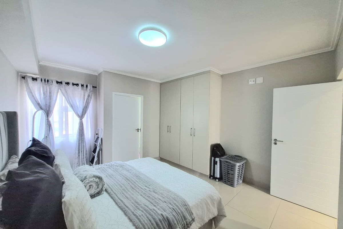 A well-maintained bedroom featuring neutral tiled flooring, built-in cupboards, and a bright, clean aesthetic.