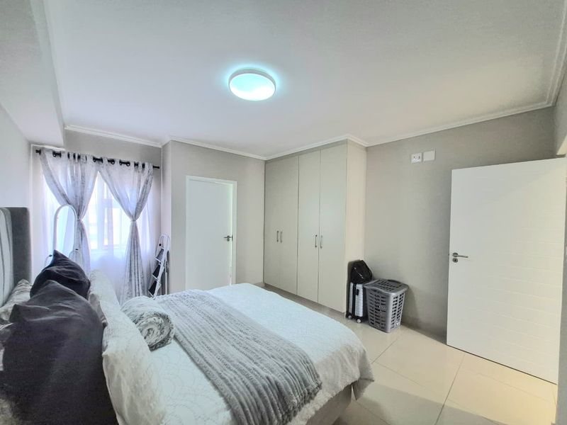 A well-maintained bedroom featuring neutral tiled flooring, built-in cupboards, and a bright, clean aesthetic.