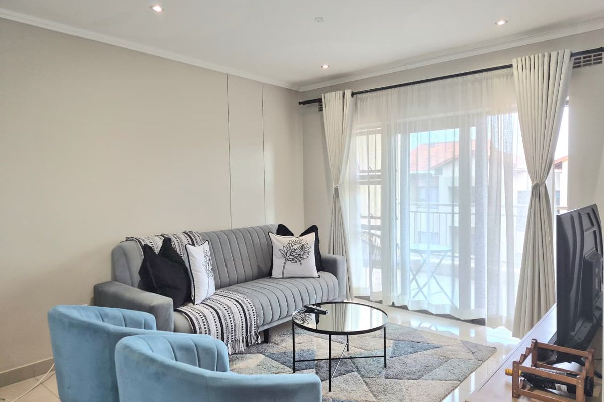 A bright and modern living room featuring tiled floors, recessed downlighting, and a large sliding glass door providing access to the balcony.
