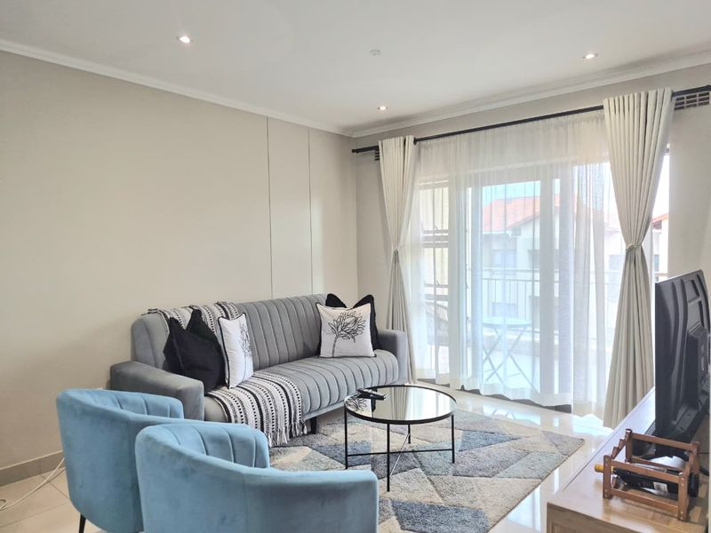 A bright and modern living room featuring tiled floors, recessed downlighting, and a large sliding glass door providing access to the balcony.