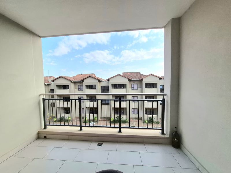 A clean, covered balcony featuring tiled flooring and a secure metal balustrade, offering an open view of the surrounding apartment complex.