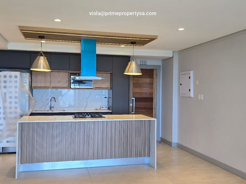 Modern kitchen featuring a central island with a gas hob, sleek cabinetry, stone countertops, and integrated lighting in a contemporary open-plan layout.