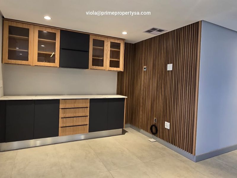 Modern kitchen area featuring sleek two-tone cabinetry, stone countertops, and decorative slatted wood wall paneling with recessed lighting.